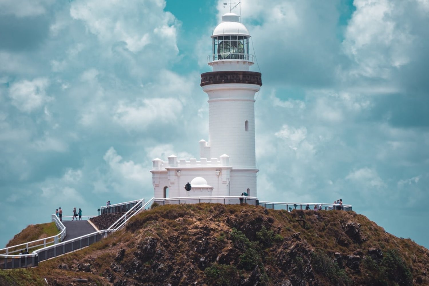 white lighthouse on brown hill under blue sky and white clouds during daytime